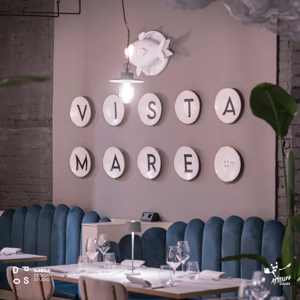Parete «Vista mare» con piatti in ceramica e divanetti in velluto blu a Krudo